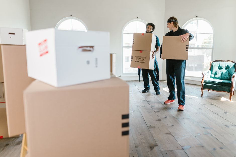 Two crew members carrying boxes through a bright living room